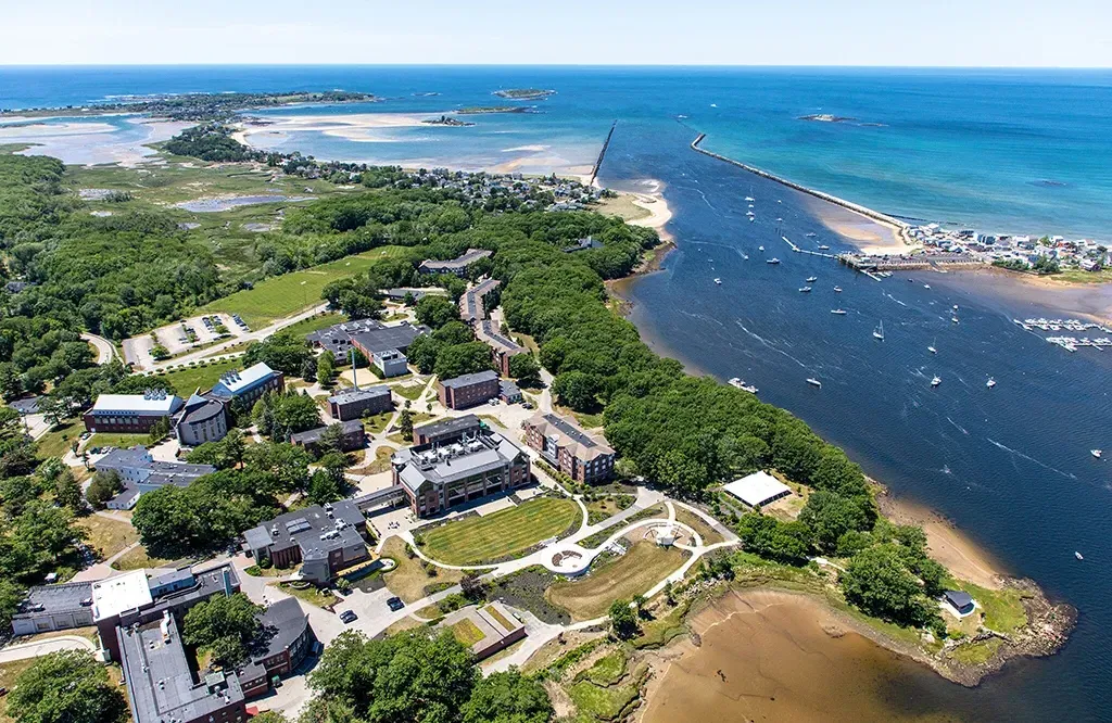 An aerial view of the U N E Biddeford Campus including the brick buildings, coastline, and ocean